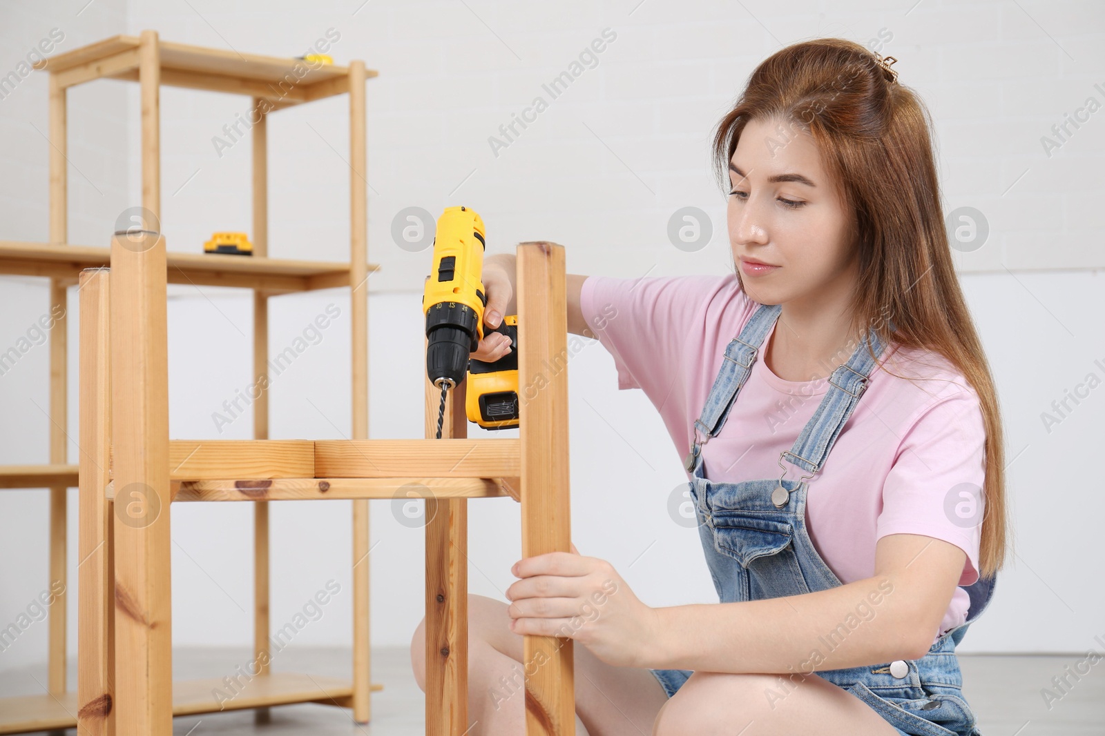 Photo of Woman with electric screwdriver assembling furniture indoors