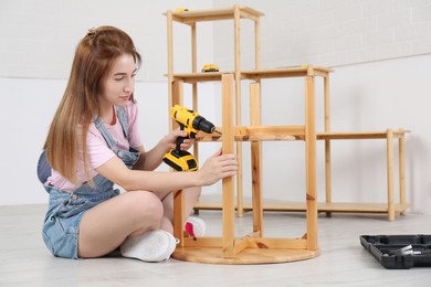 Woman with electric screwdriver assembling table on floor at home