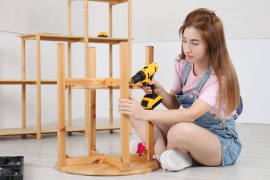 Photo of Woman with electric screwdriver assembling table on floor at home