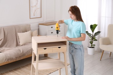 Woman with electric screwdriver assembling table in room