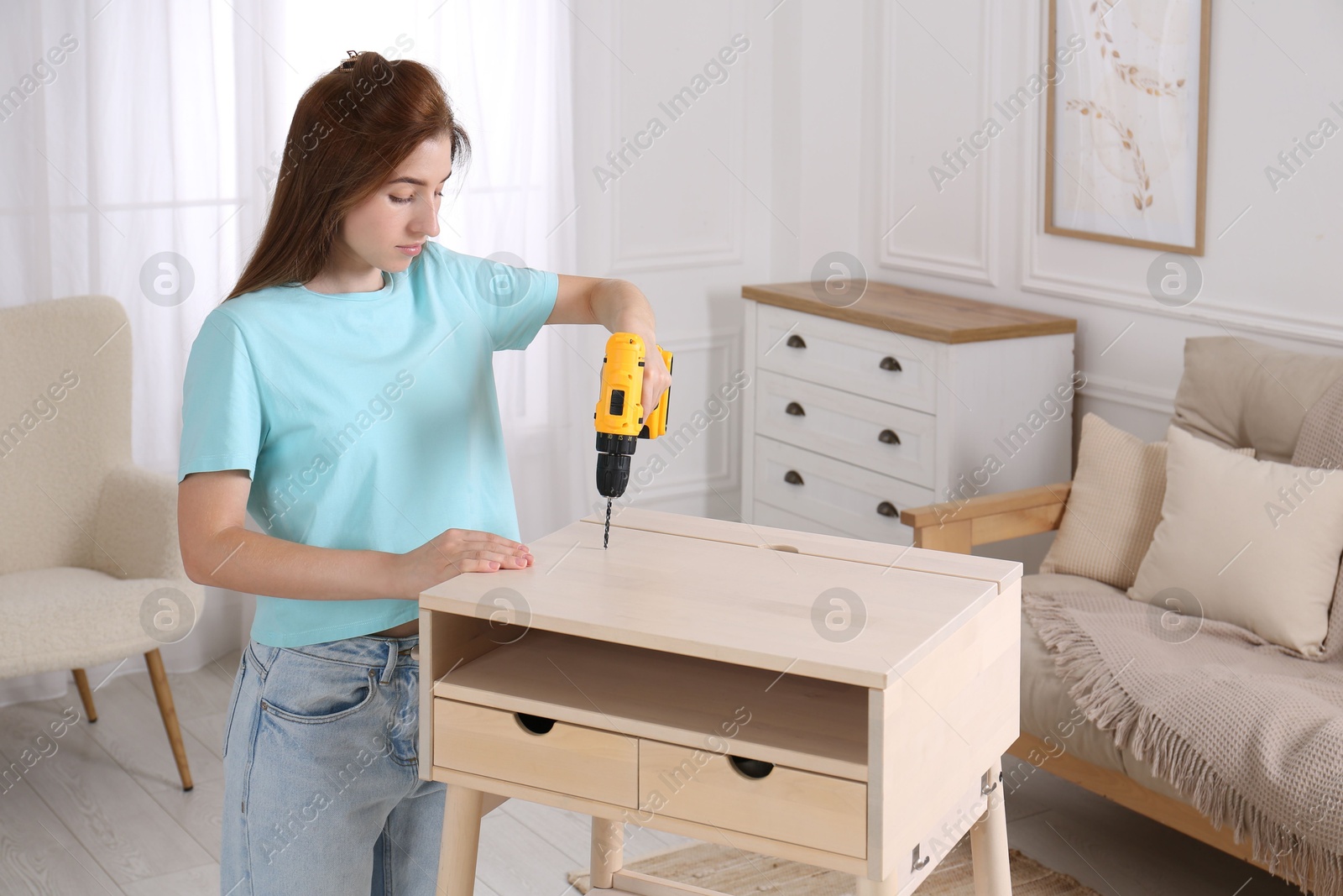 Photo of Woman with electric screwdriver assembling table in room