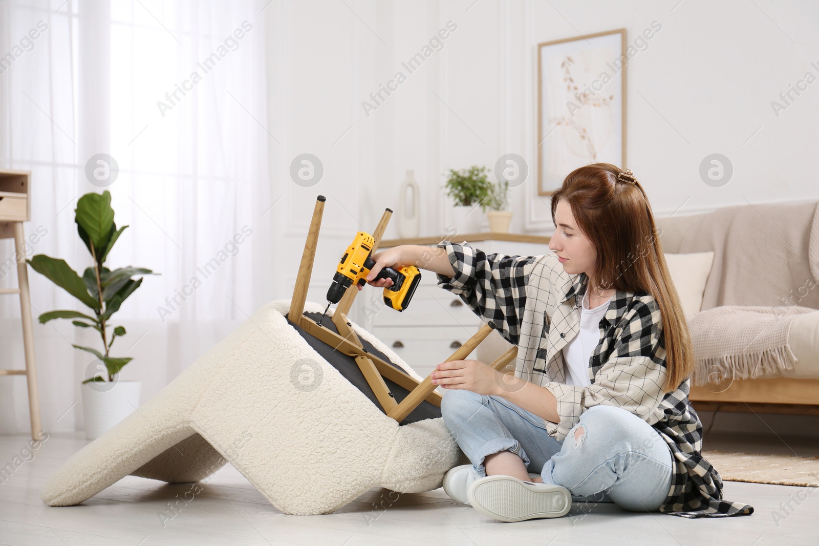 Photo of Woman with electric screwdriver assembling armchair at home