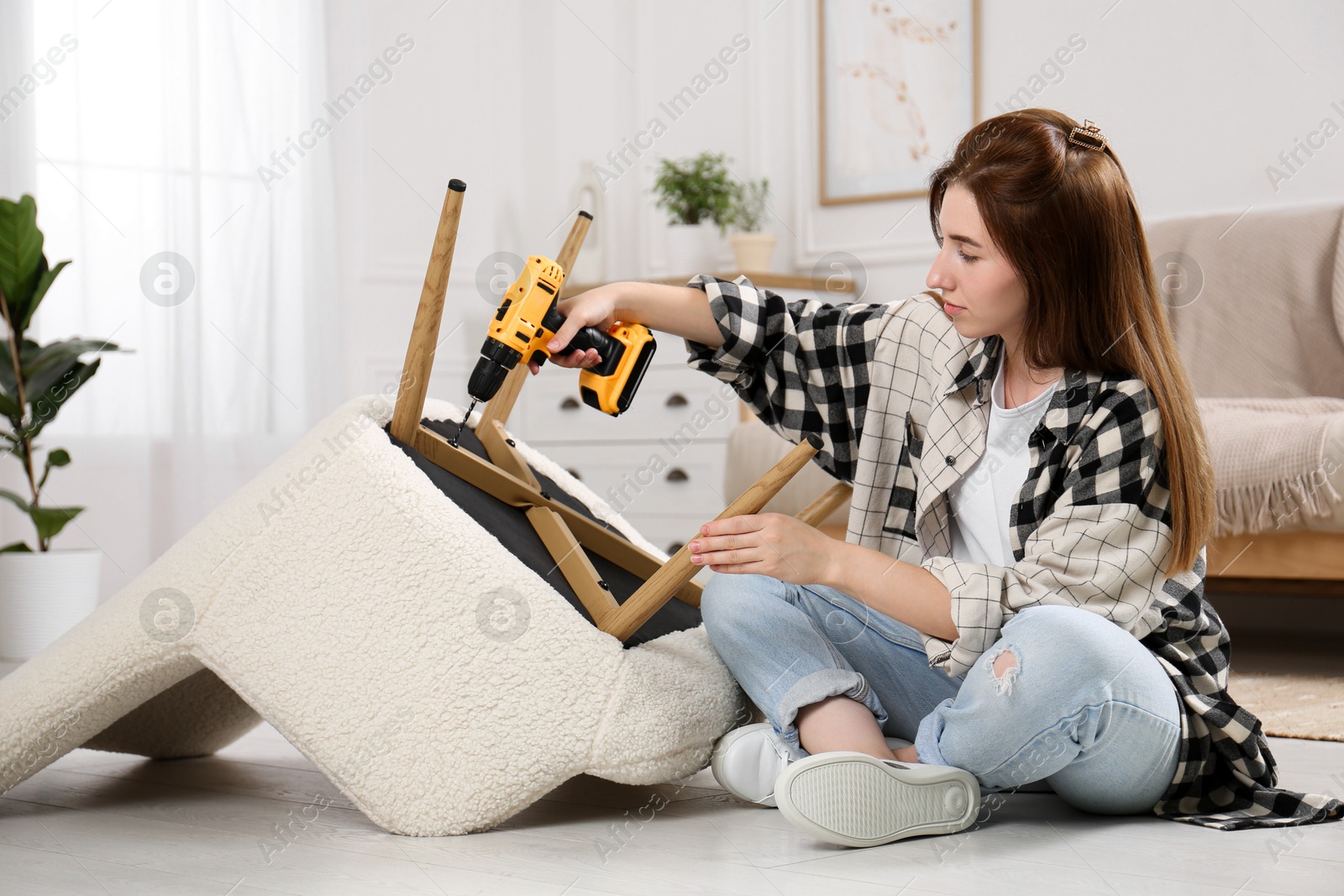 Photo of Woman with electric screwdriver assembling armchair at home