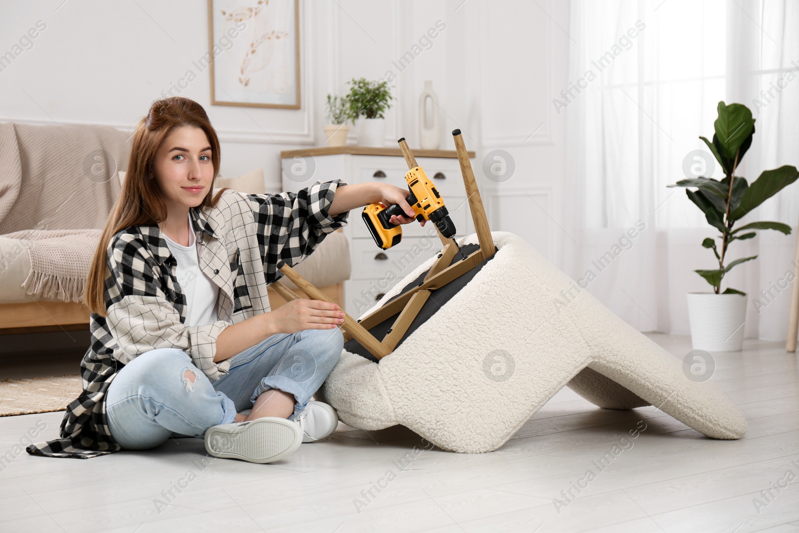 Photo of Woman with electric screwdriver assembling armchair at home