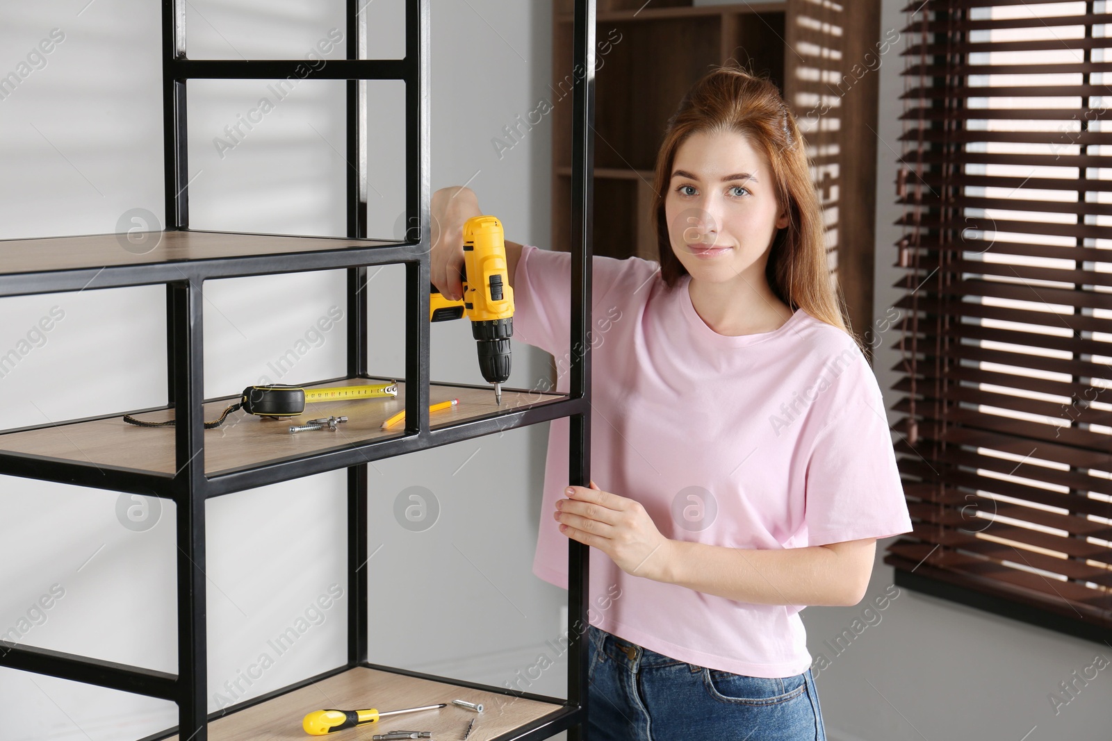 Photo of Woman with electric screwdriver assembling shelving unit in room