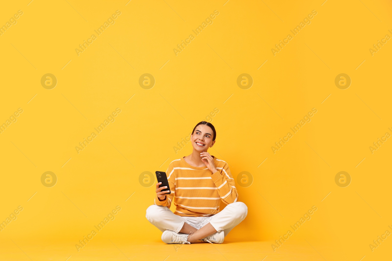 Photo of Happy woman with smartphone on yellow background