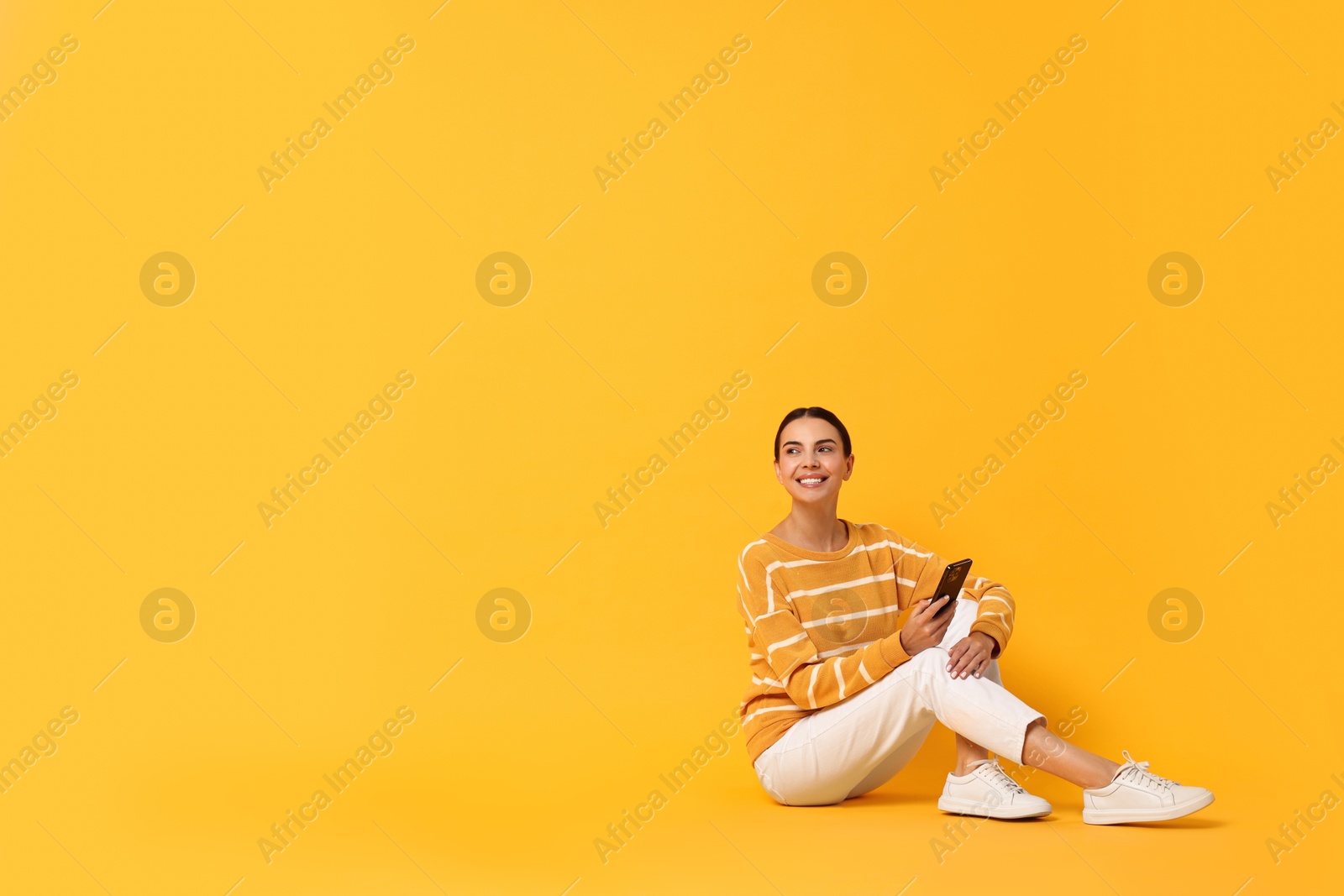 Photo of Happy woman with smartphone on yellow background. Space for text