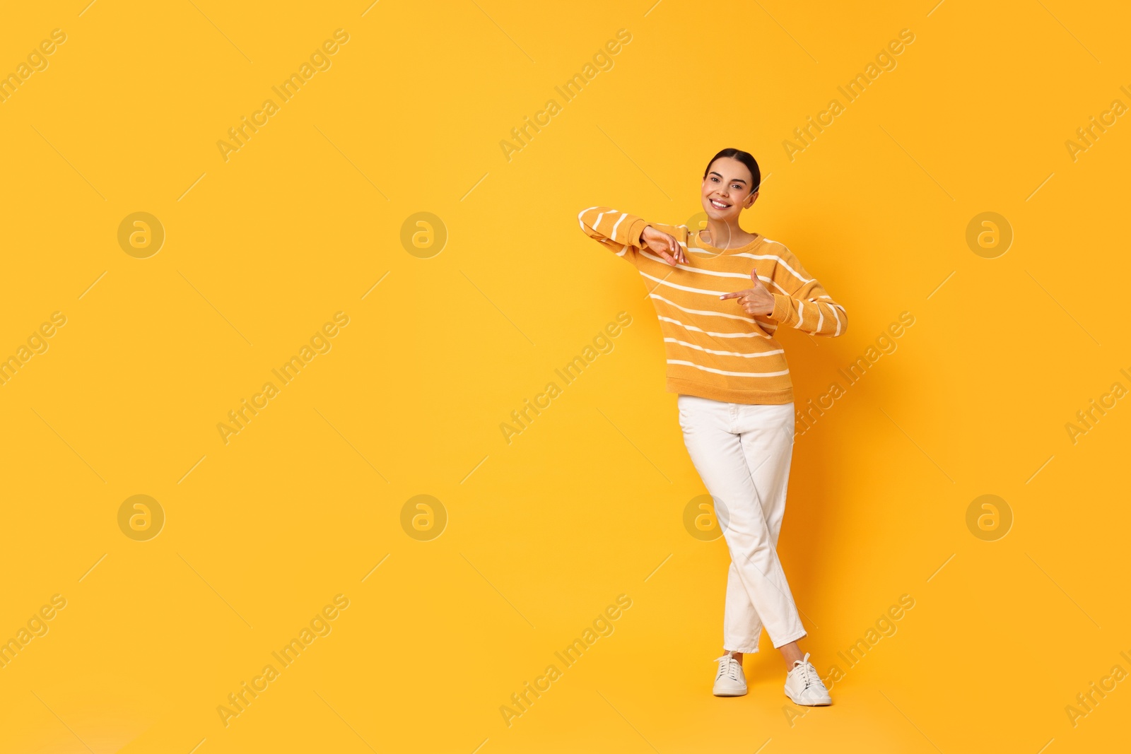 Photo of Smiling woman pointing at something on yellow background. Space for text