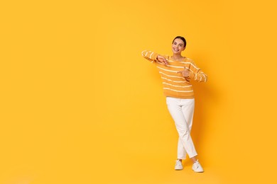 Smiling woman pointing at something on yellow background. Space for text