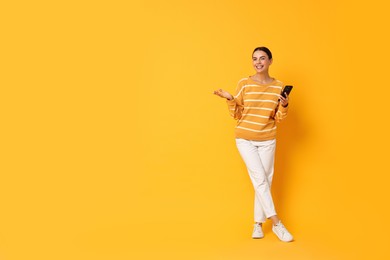 Smiling woman with smartphone on yellow background. Space for text