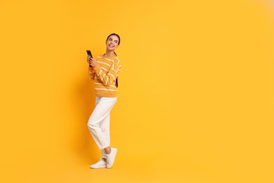 Photo of Smiling woman with smartphone on yellow background. Space for text