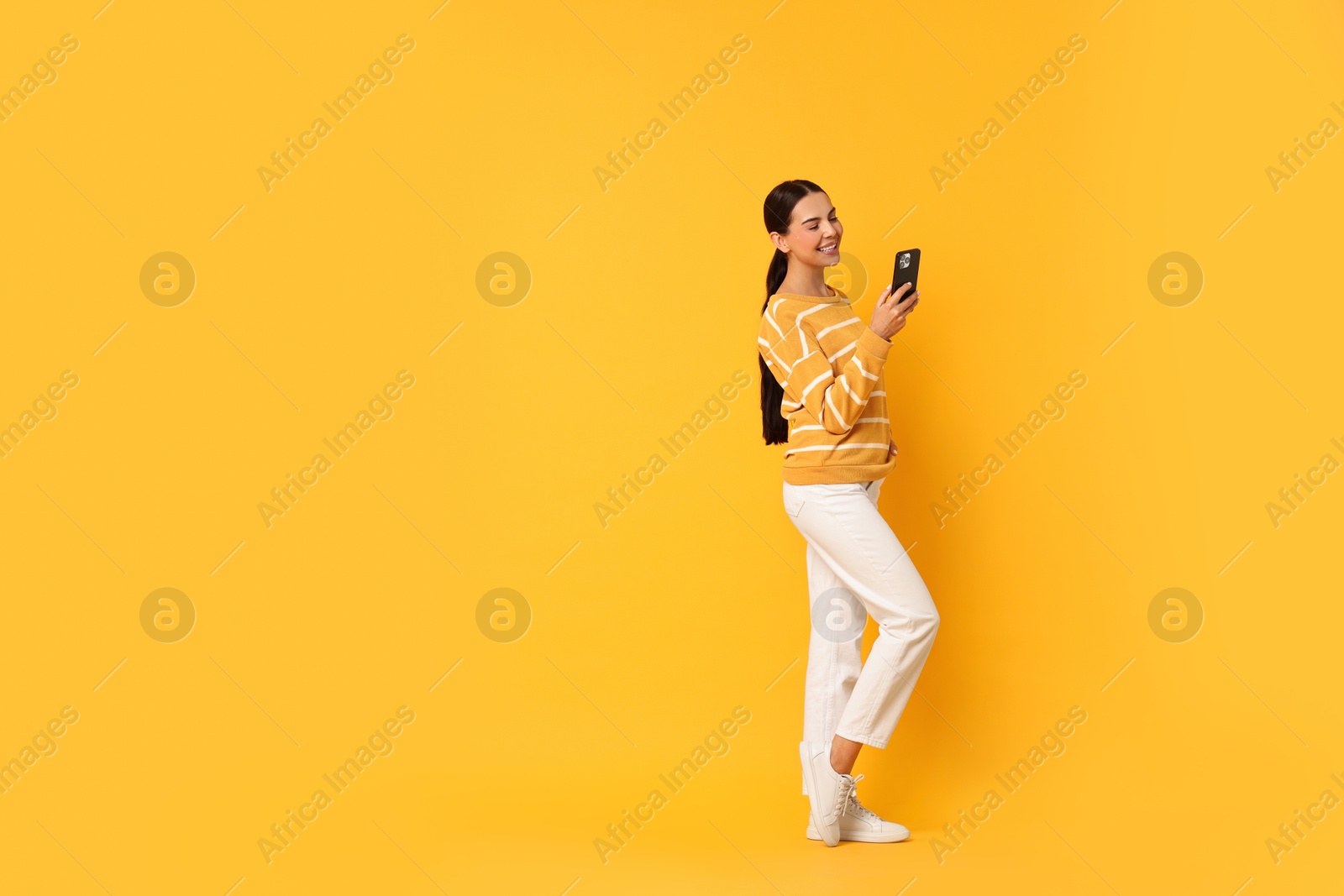 Photo of Smiling woman with smartphone on yellow background. Space for text