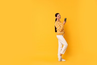 Smiling woman with smartphone on yellow background. Space for text