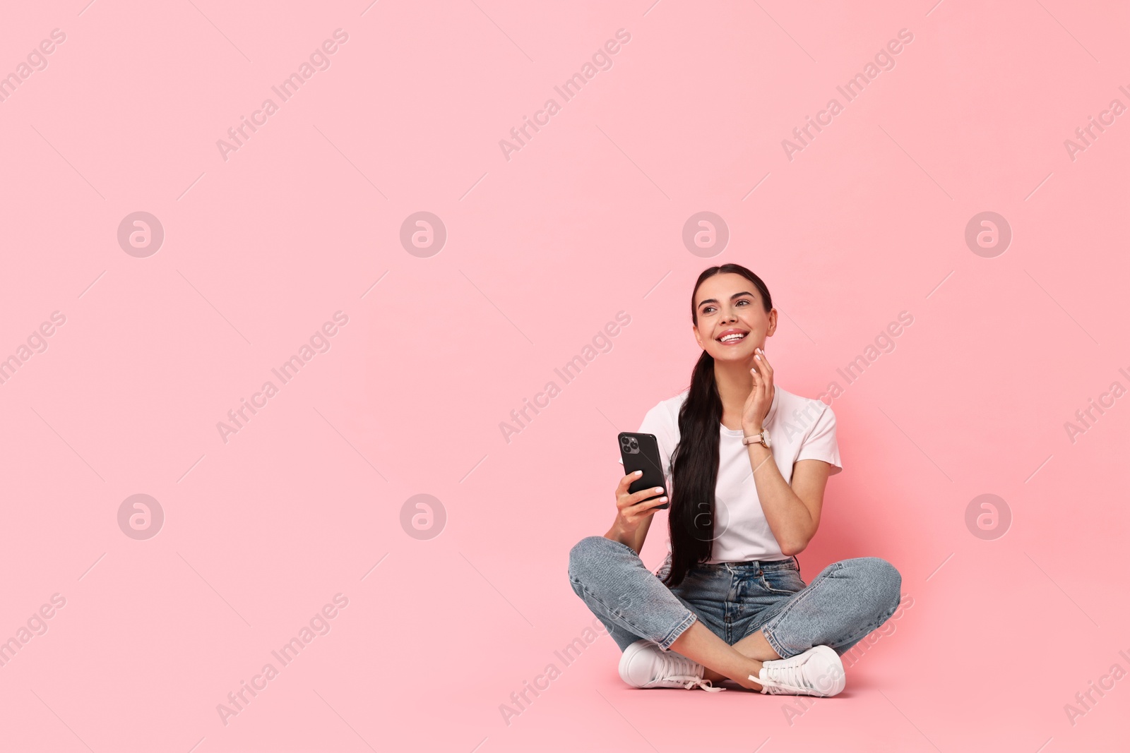 Photo of Smiling woman with smartphone on pink background. Space for text