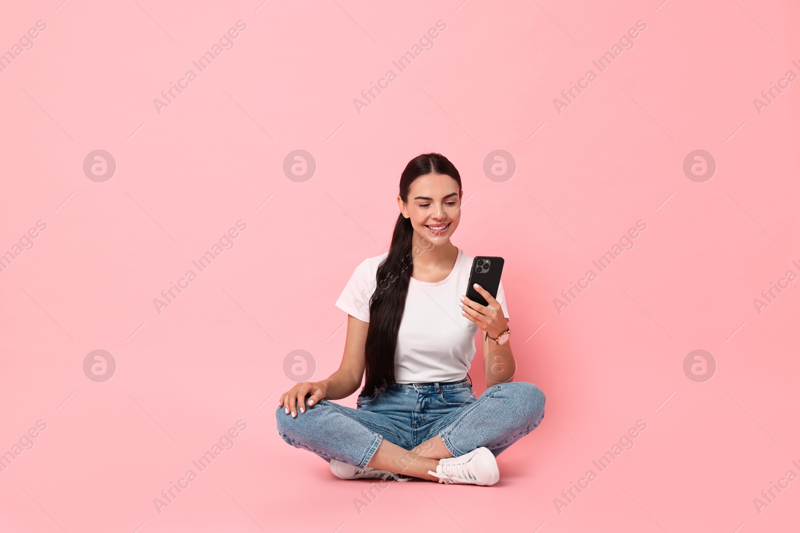 Photo of Smiling woman with smartphone on pink background