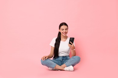 Photo of Smiling woman with smartphone on pink background