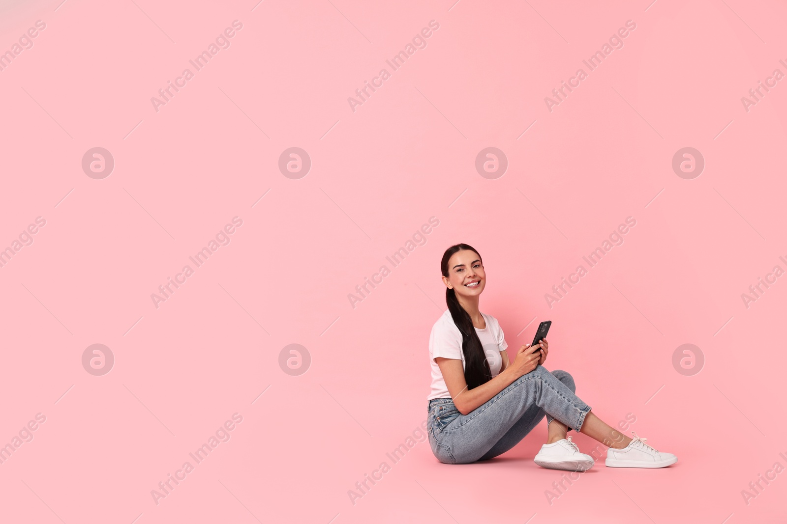 Photo of Smiling woman with smartphone on pink background. Space for text