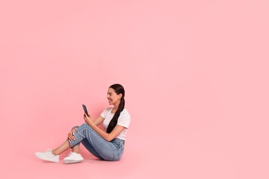 Photo of Smiling woman with smartphone on pink background. Space for text