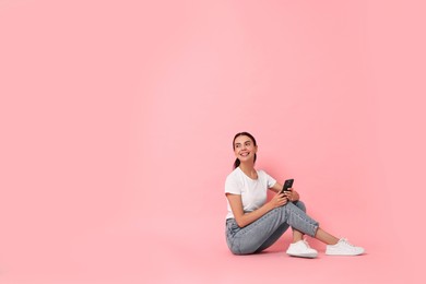 Smiling woman with smartphone on pink background. Space for text