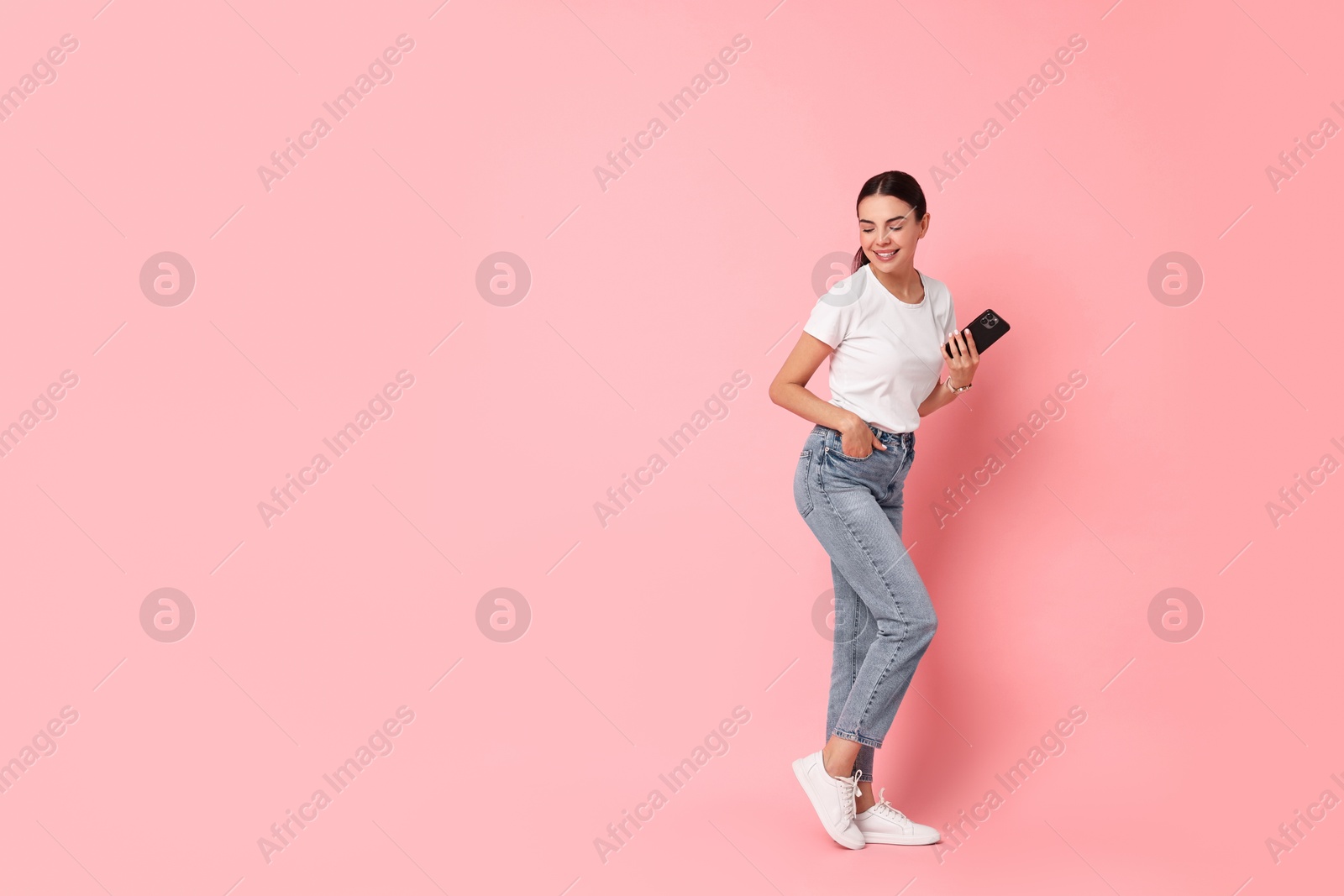 Photo of Smiling woman with smartphone on pink background. Space for text