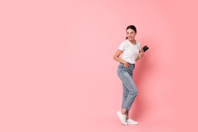 Smiling woman with smartphone on pink background. Space for text