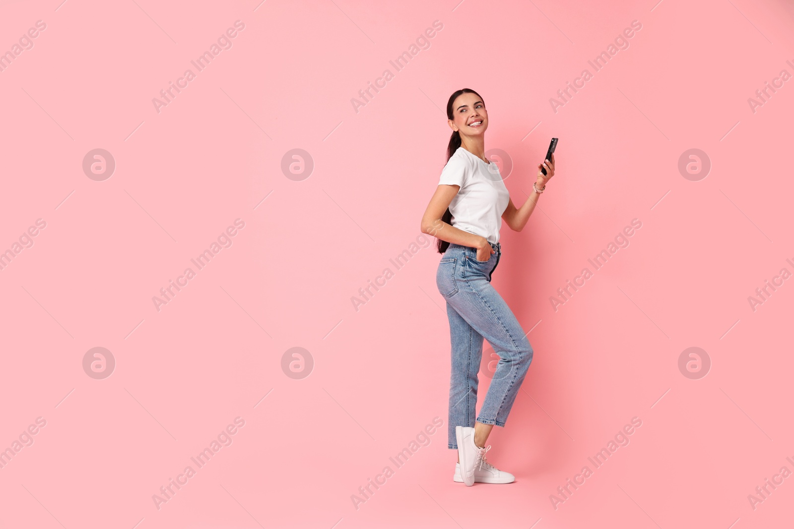 Photo of Smiling woman with smartphone on pink background. Space for text