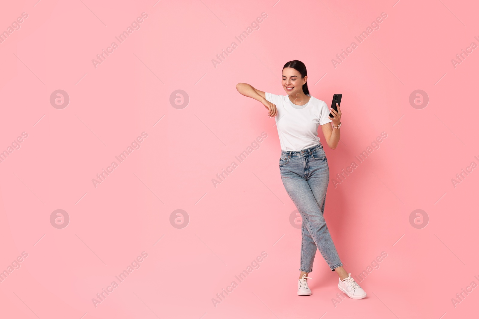 Photo of Smiling woman with smartphone on pink background. Space for text