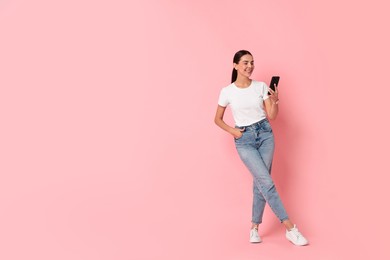 Photo of Smiling woman with smartphone on pink background. Space for text