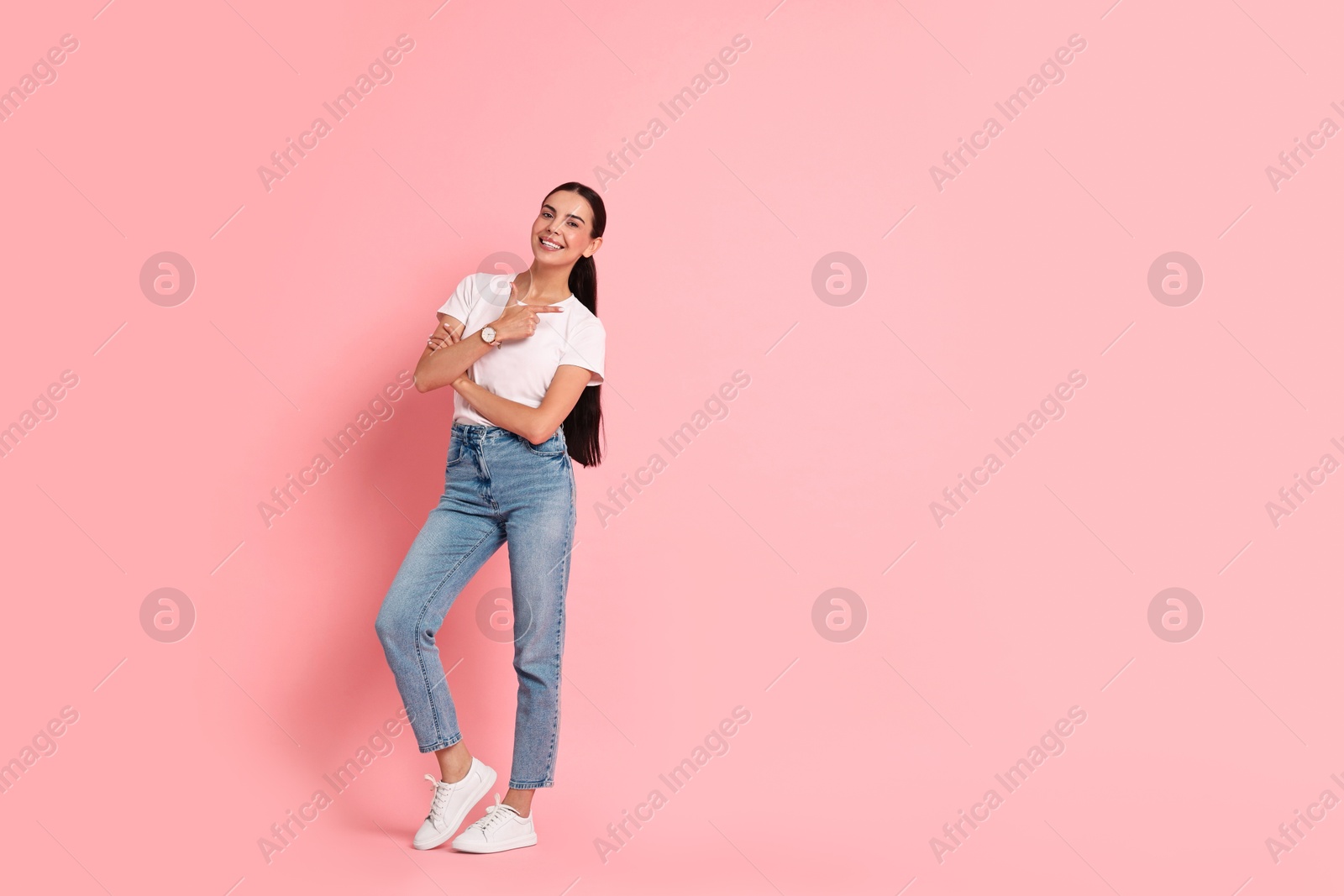 Photo of Smiling woman pointing at something on pink background. Space for text