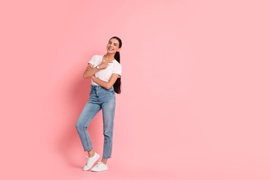 Photo of Smiling woman pointing at something on pink background. Space for text