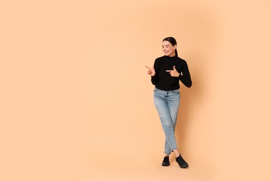 Photo of Smiling woman pointing at something on beige background. Space for text