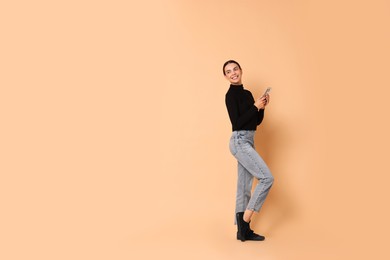 Smiling woman with smartphone on beige background. Space for text