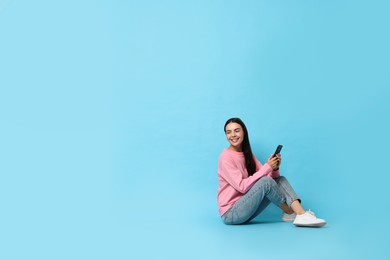 Photo of Smiling woman with smartphone on light blue background. Space for text