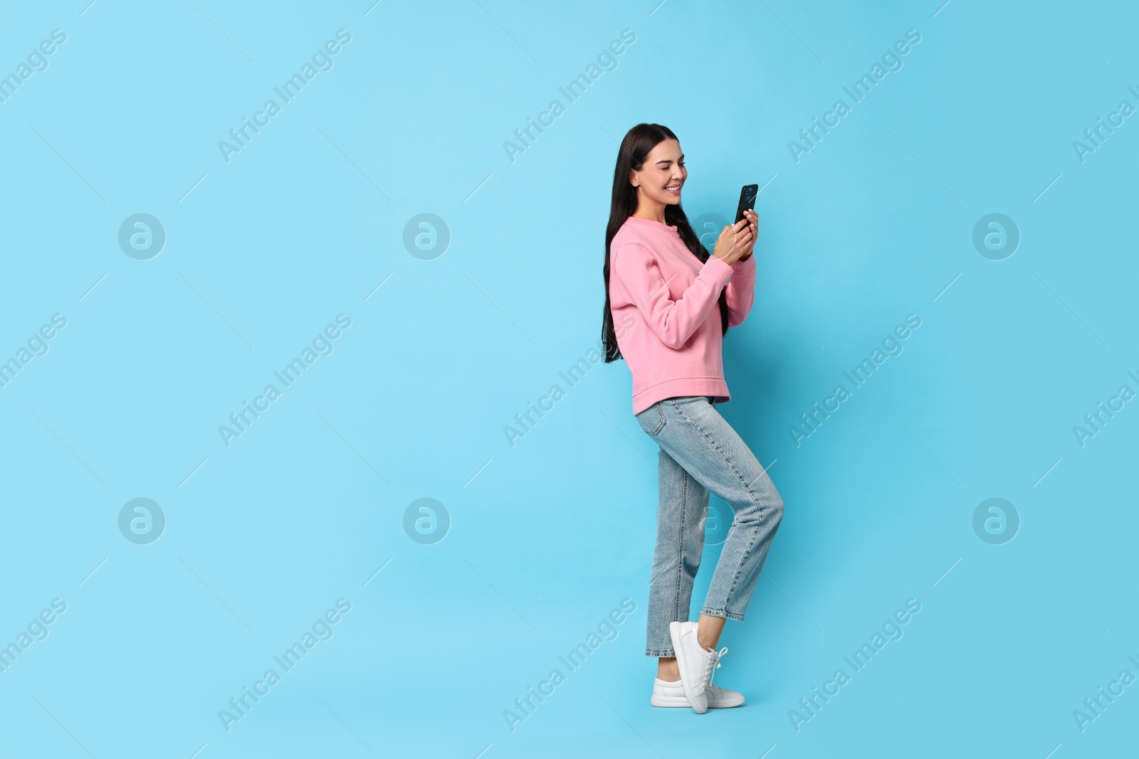 Photo of Smiling woman with smartphone on light blue background. Space for text