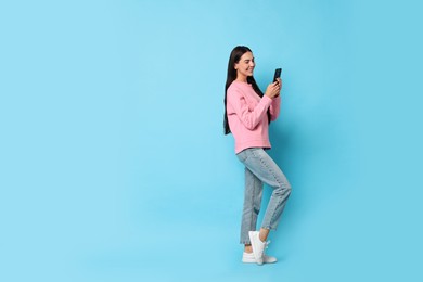 Photo of Smiling woman with smartphone on light blue background. Space for text