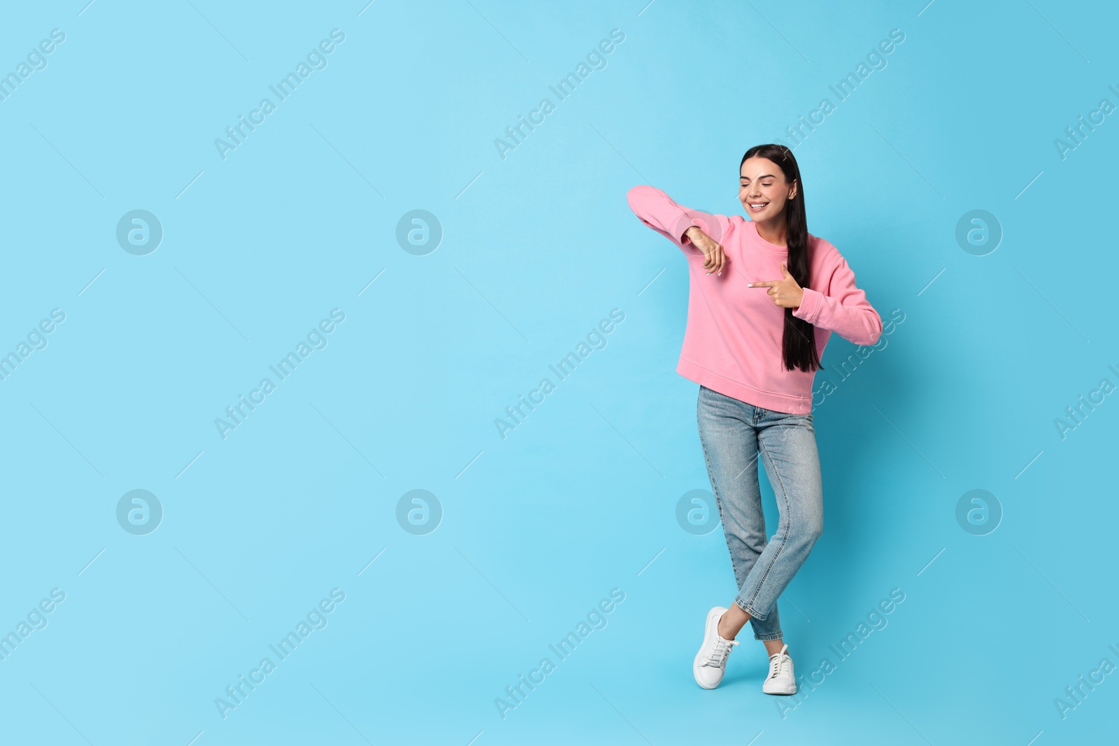 Photo of Smiling woman pointing at something on light blue background. Space for text