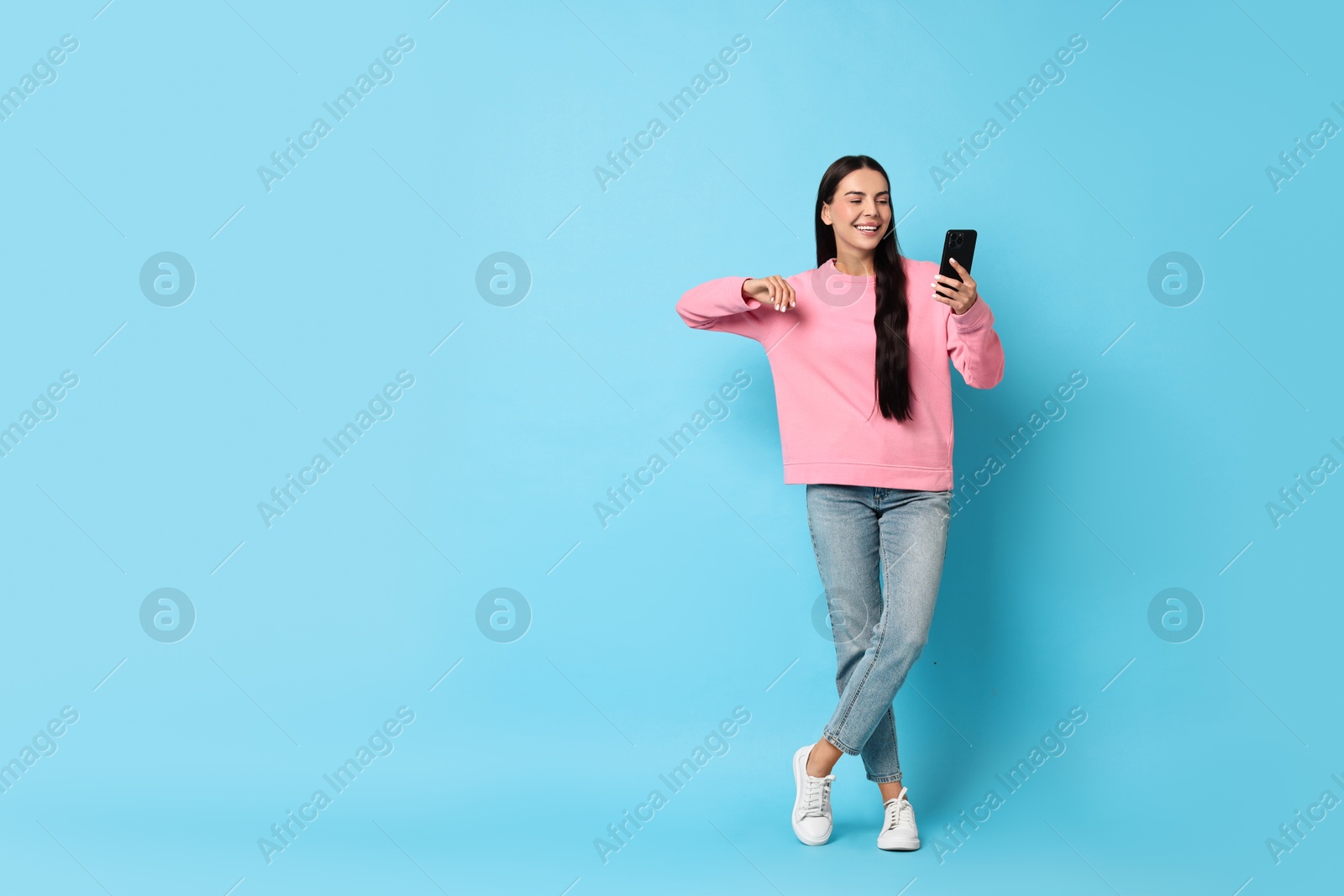 Photo of Smiling woman with smartphone on light blue background. Space for text