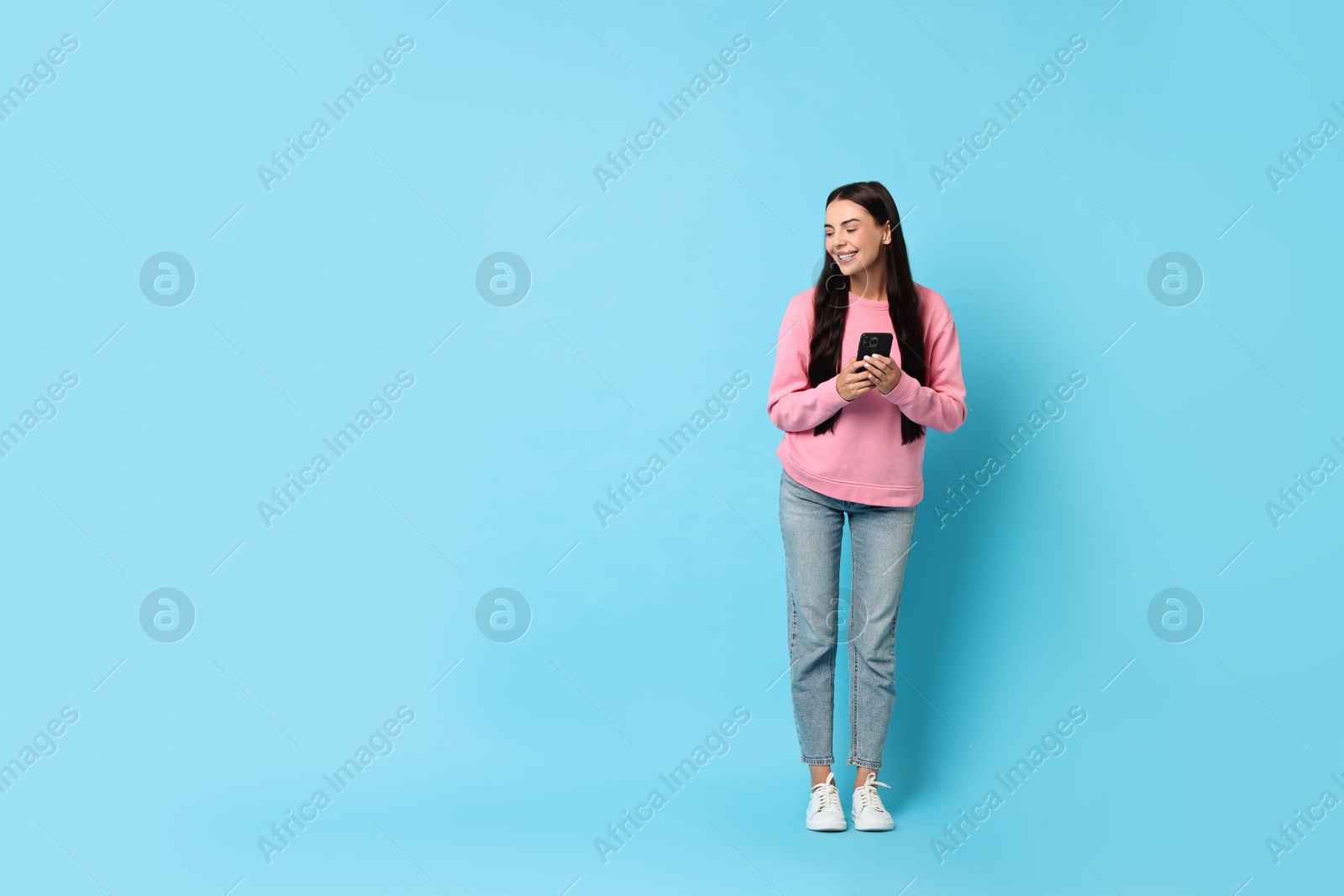 Photo of Smiling woman with smartphone on light blue background. Space for text