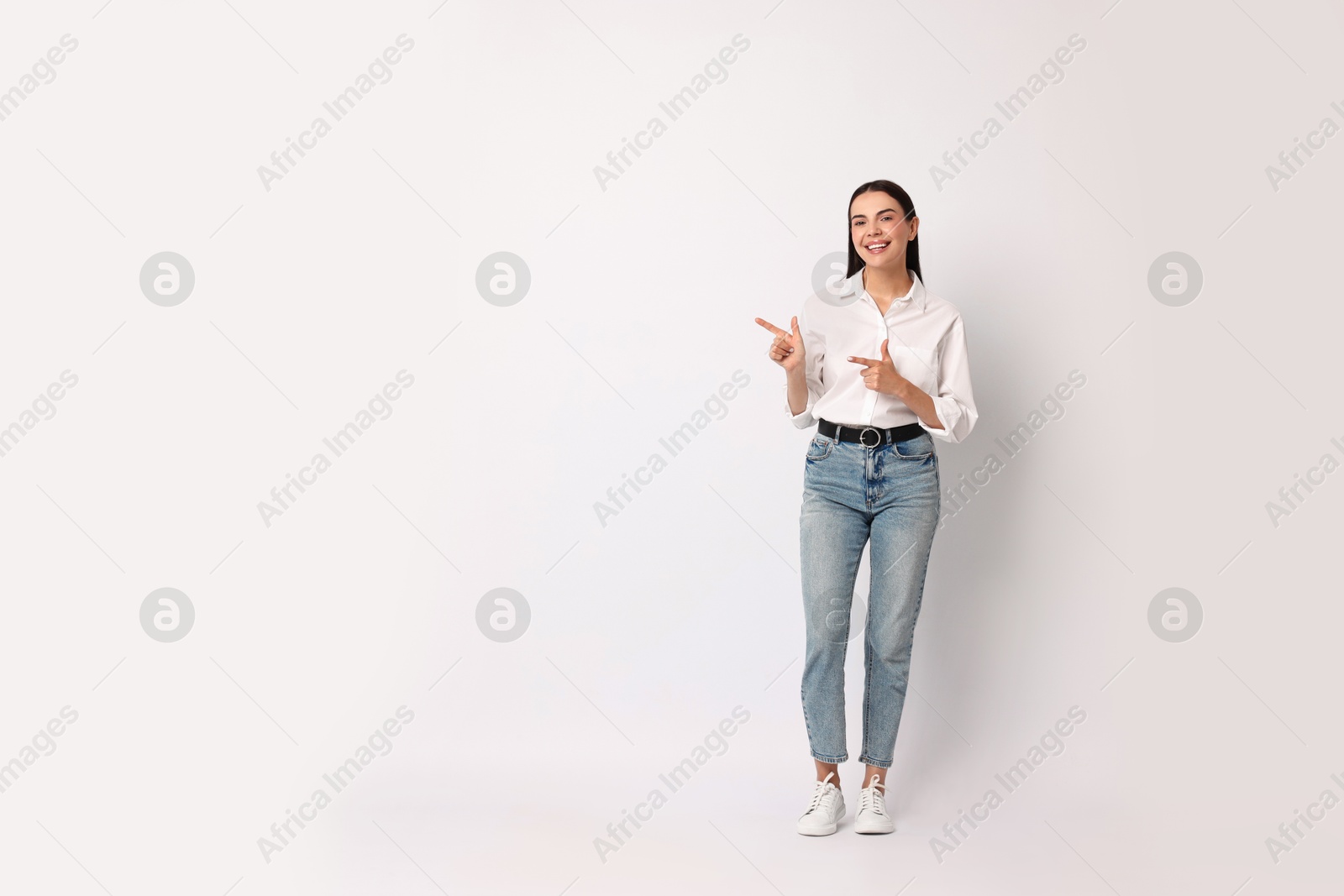 Photo of Smiling woman pointing at something on white background. Space for text