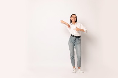 Photo of Smiling woman pointing at something on white background. Space for text