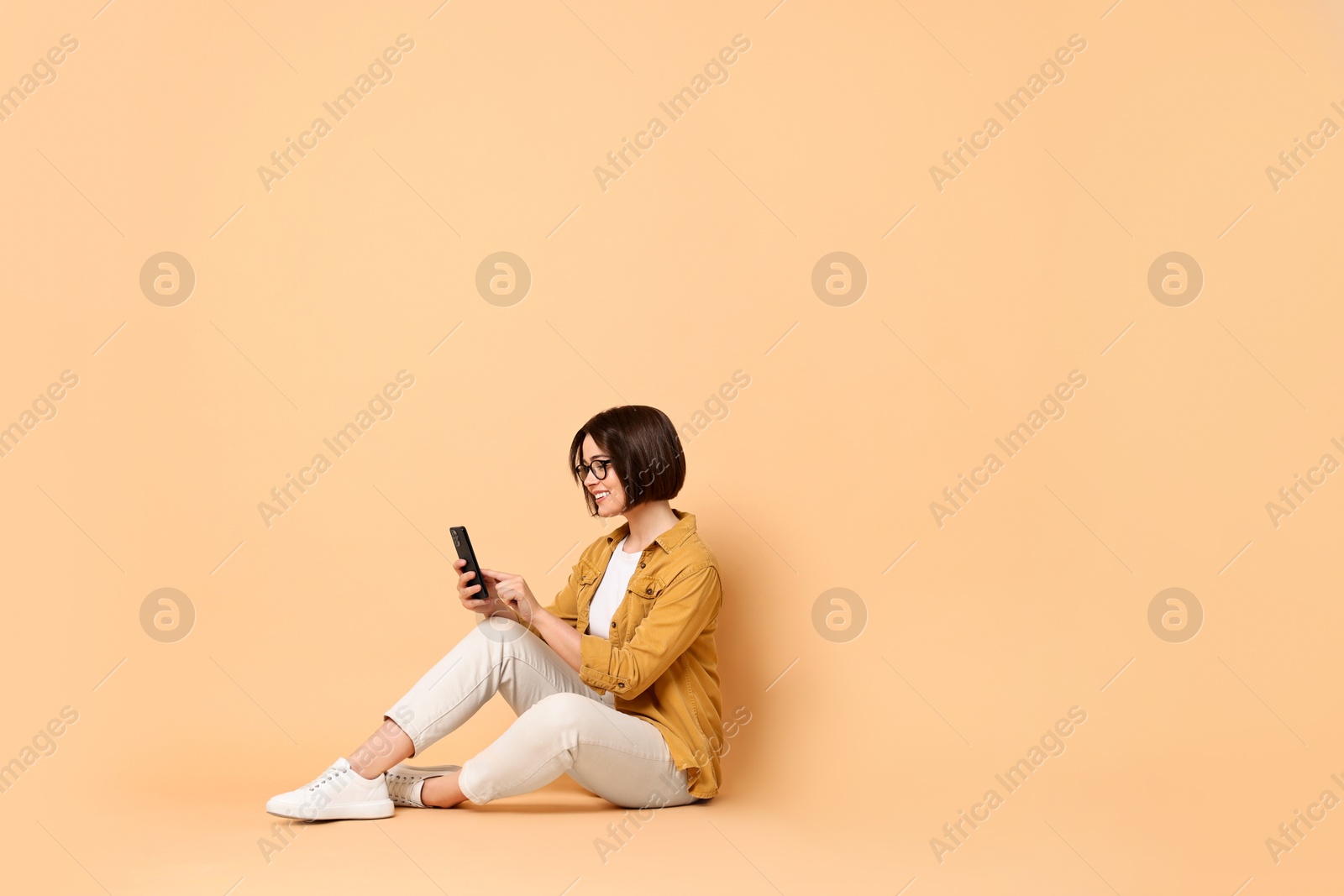 Photo of Smiling woman with smartphone sitting on beige background. Space for text