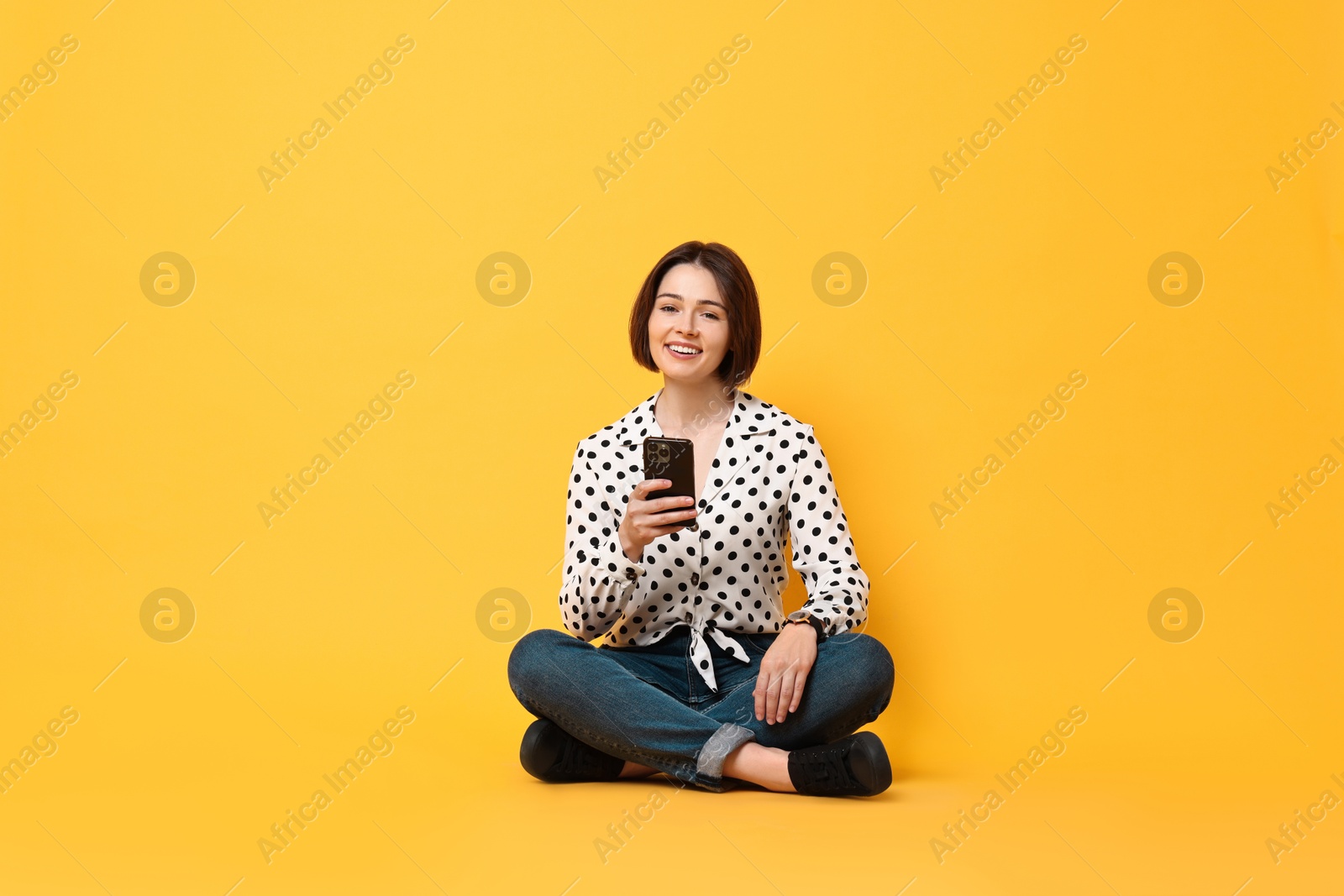 Photo of Smiling woman with smartphone sitting on yellow background