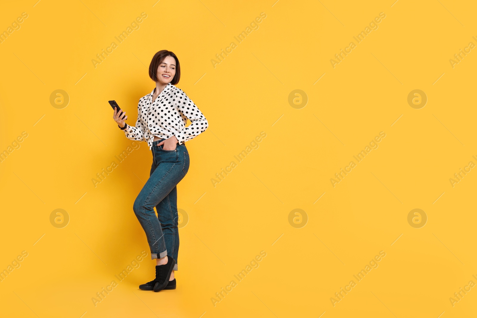 Photo of Smiling woman with smartphone on yellow background. Space for text