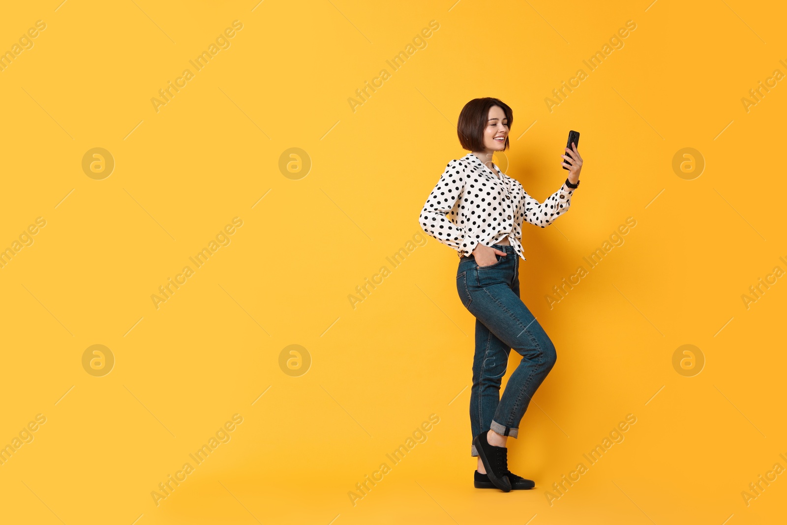 Photo of Smiling woman with smartphone on yellow background. Space for text