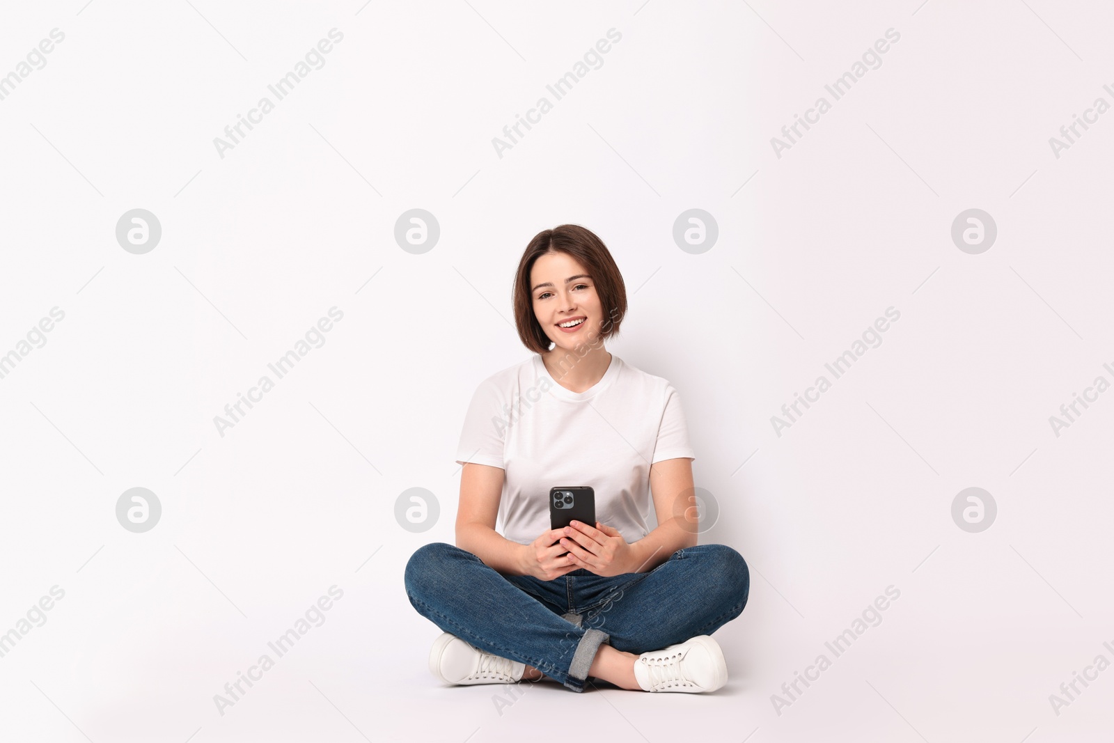 Photo of Smiling woman with smartphone sitting on white background