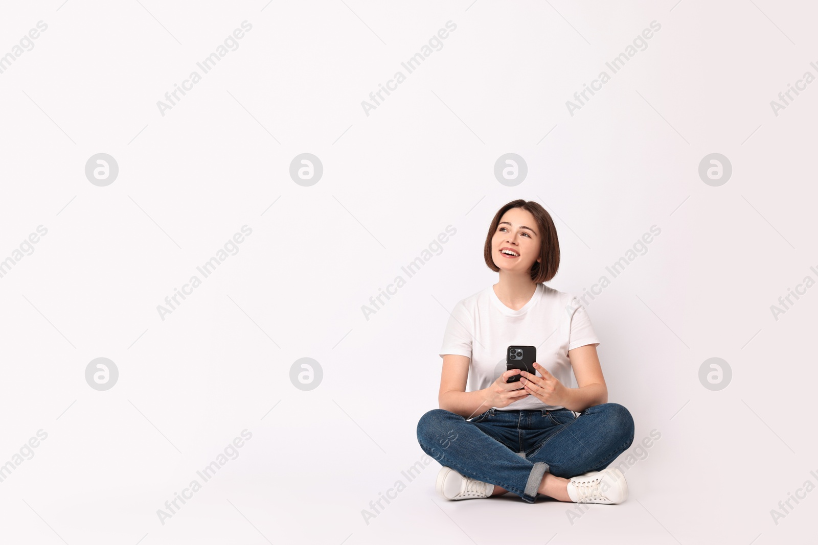 Photo of Smiling woman with smartphone sitting on white background. Space for text