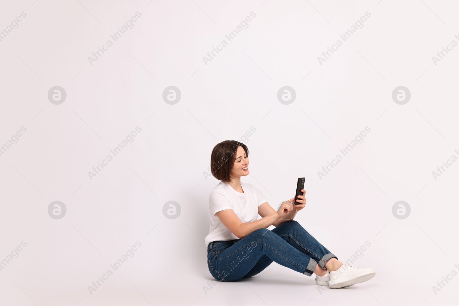 Photo of Smiling woman with smartphone sitting on white background. Space for text