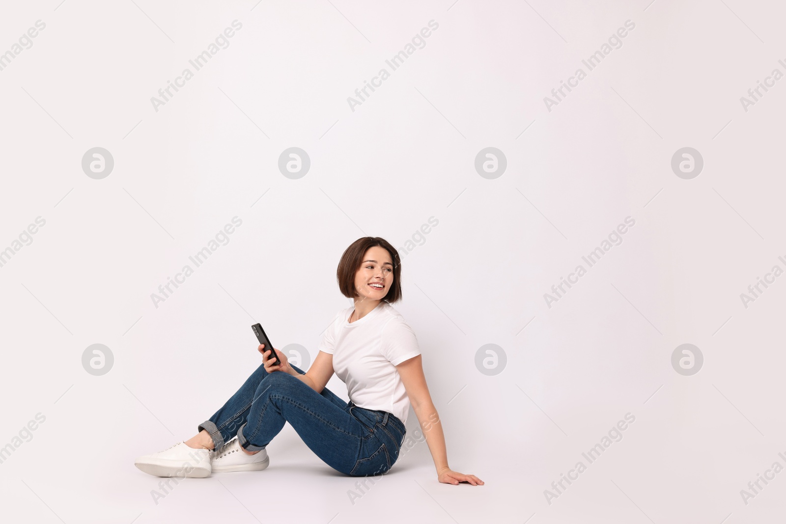 Photo of Smiling woman with smartphone sitting on white background. Space for text