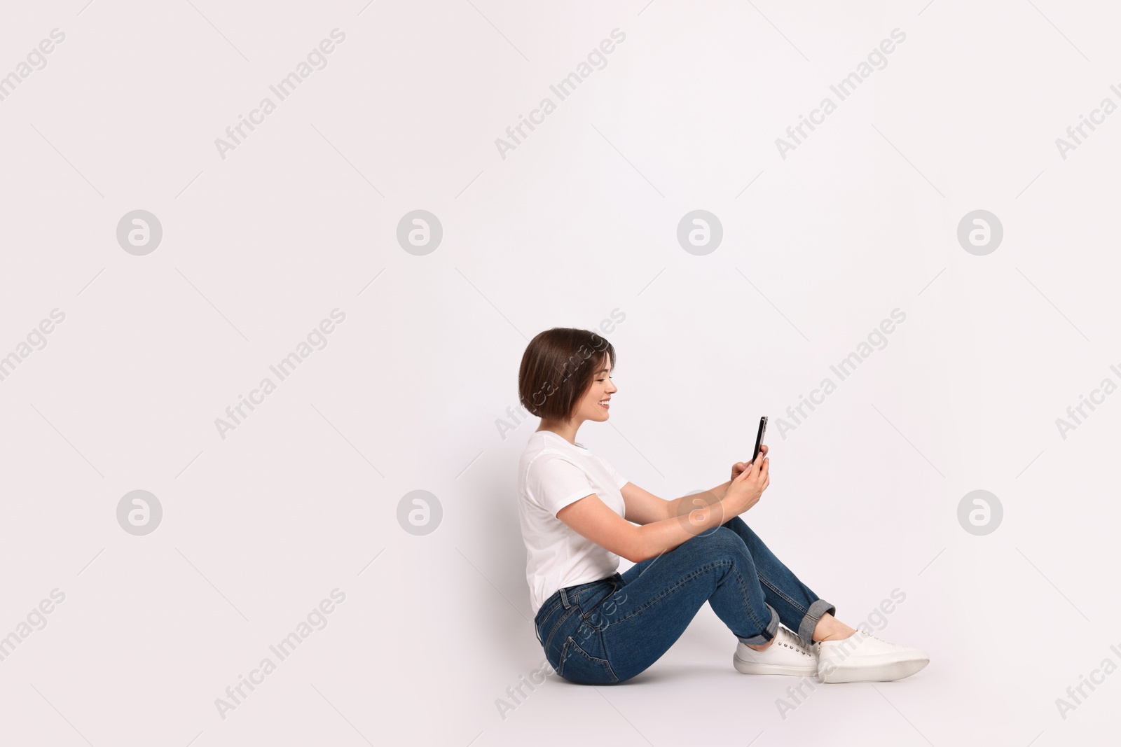 Photo of Smiling woman with smartphone sitting on white background. Space for text