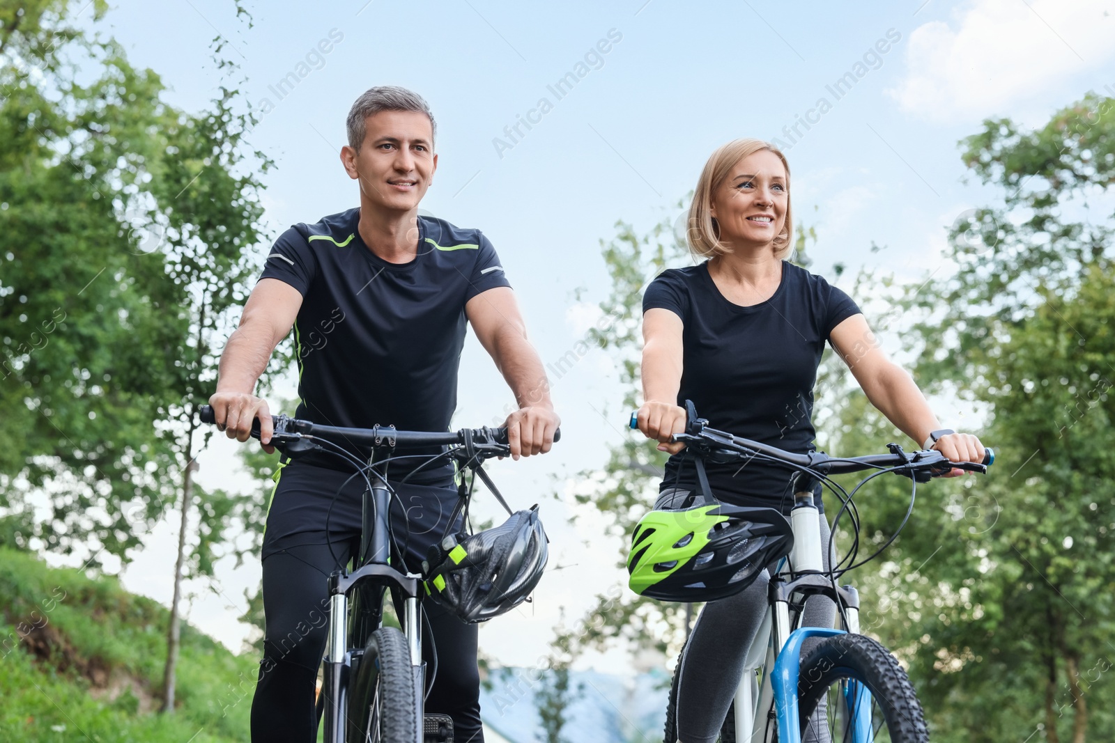 Photo of Happy couple with bicycles in park, low angle view